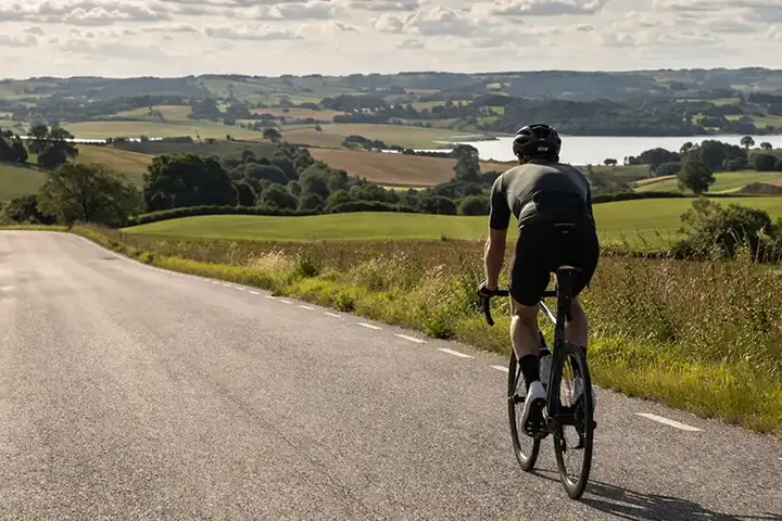 Lange danske landevejskilometer med cykelrytter, åbent landskab og tydelig langturstemning.