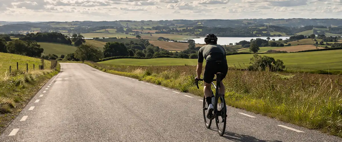 Lange danske landevejskilometer med cykelrytter, åbent landskab og tydelig langturstemning.