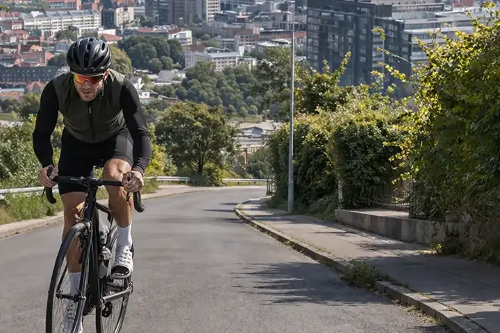 Cyklist på kuperet vej i Aarhus med udsigt mod byen og en markant bakke i baggrunden.