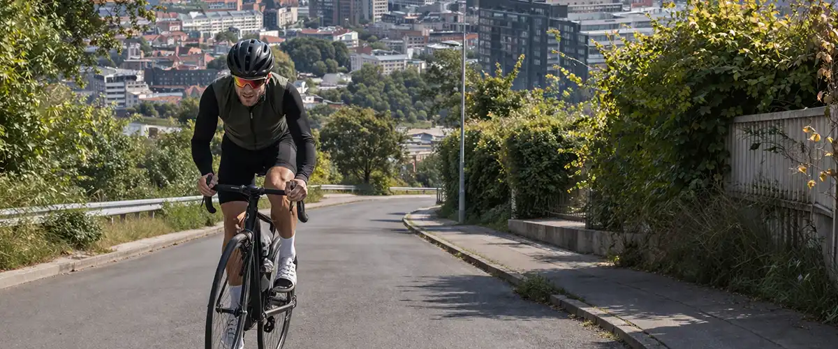 Cyklist på kuperet vej i Aarhus med udsigt mod byen og en markant bakke i baggrunden.