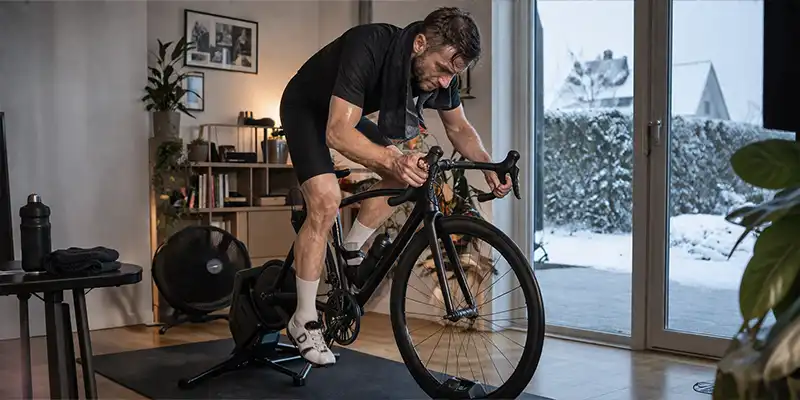 Indendørs cykeltræning med håndklæde, vandflaske og stabil belastning.