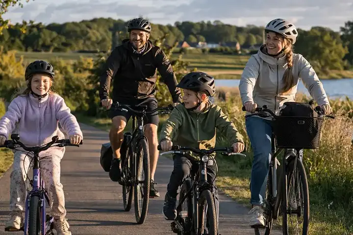 Familie på cykeltur på bred dansk sti med børn, roligt tempo og grønne omgivelser.