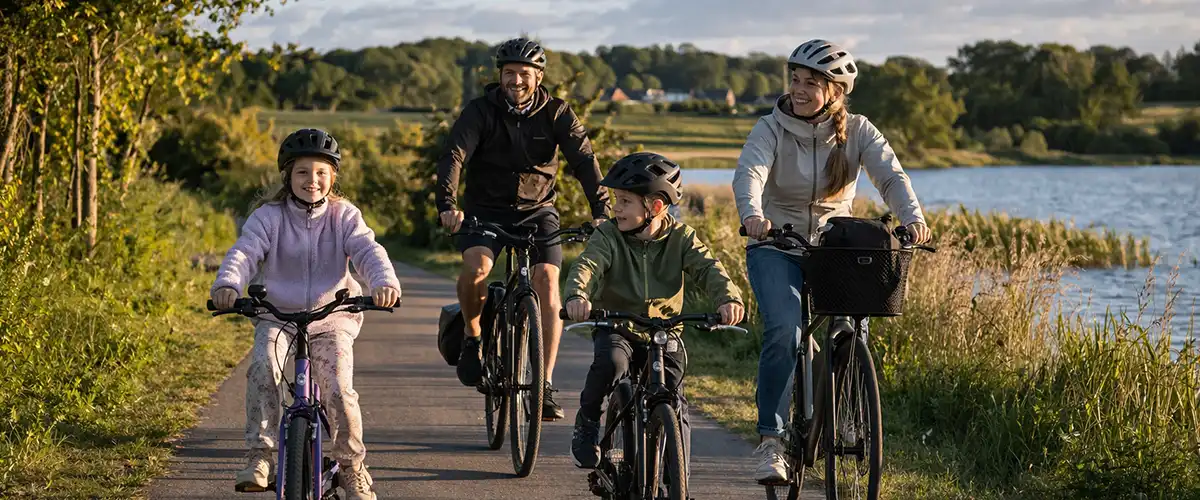 Familie på cykeltur på bred dansk sti med børn, roligt tempo og grønne omgivelser.