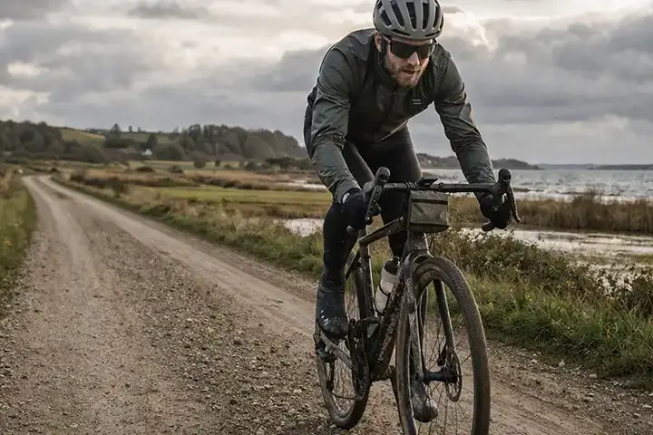 Gravelcyklist på dansk grusvej med støvet underlag, rolig natur og tydelig terrænfornemmelse.